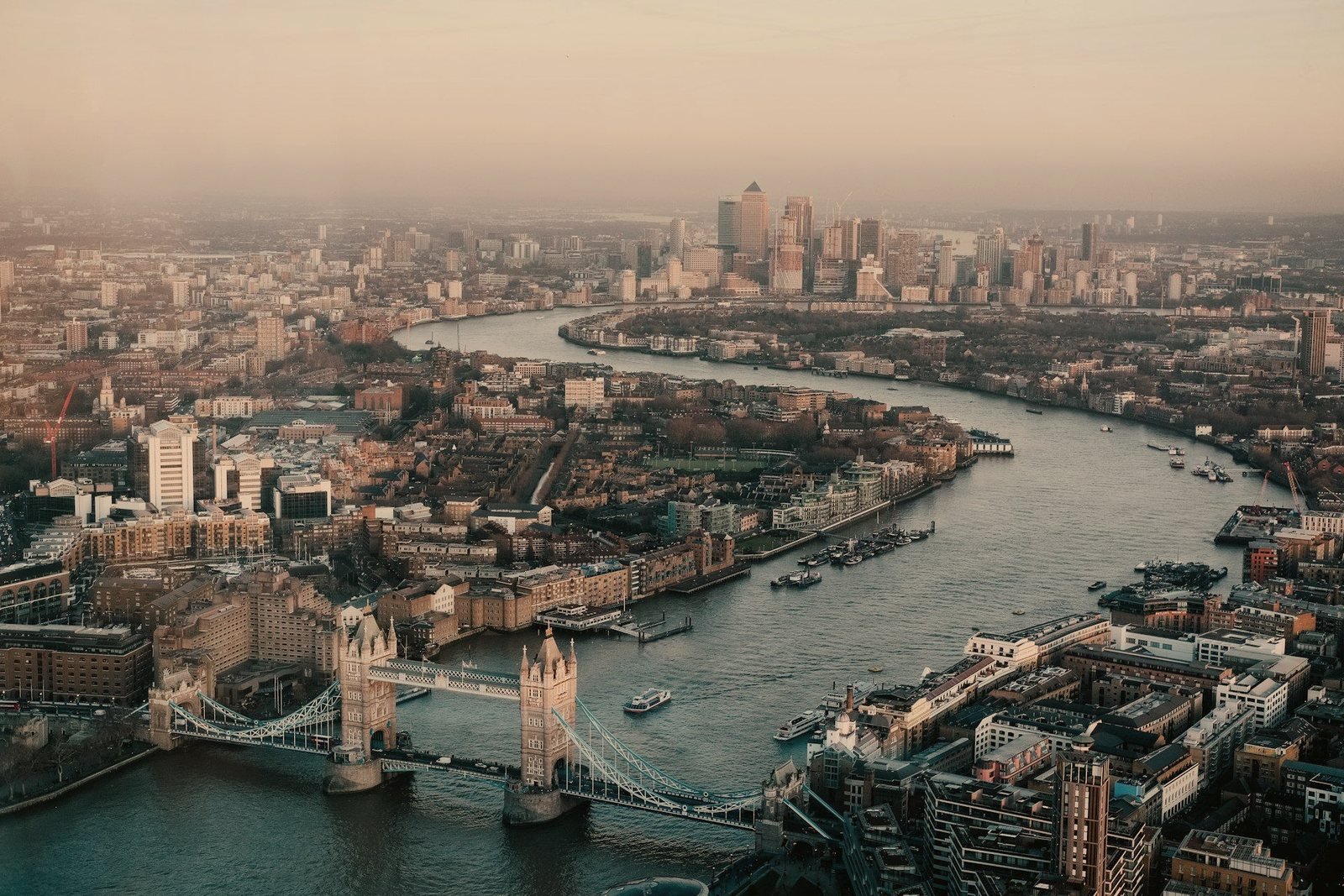 London and the Thames from the air at dusk, Tower Bridge below — plan any UK journey door to door